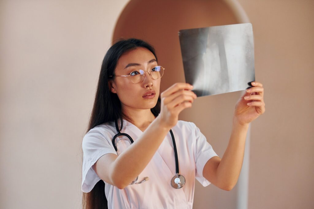 Examining x-ray. Young serious asian woman standing indoors