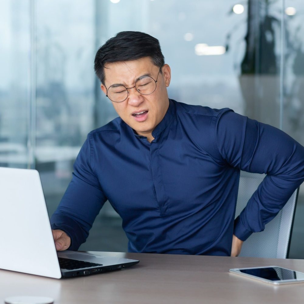 Sick overworked man at work, businessman has severe back pain, asian man holding hand on side Sick overworked man at work, businessman has severe back pain, asian man holding hand on side